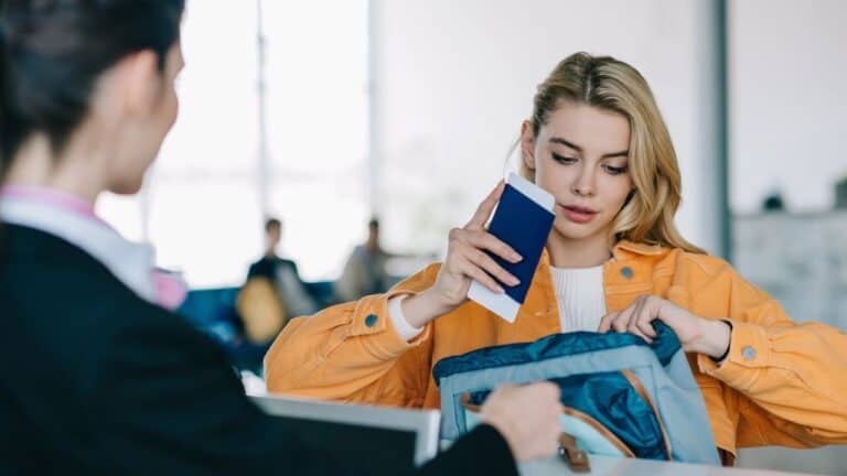 Young woman putting passport with boarding pass into bag at check-in desk in airport