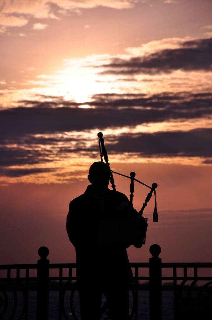 Silhouette of a bagpiper Standing Near the Metal Railings during Sunset