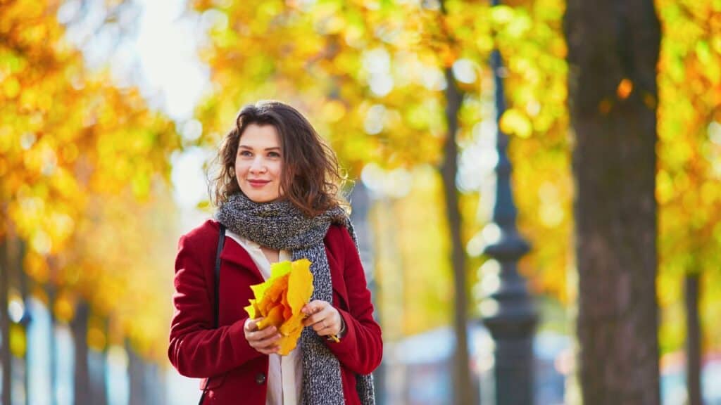 Beautiful young girl in autumn park with golden foliage on a sunny fall day, holding yellow leaves in her hands