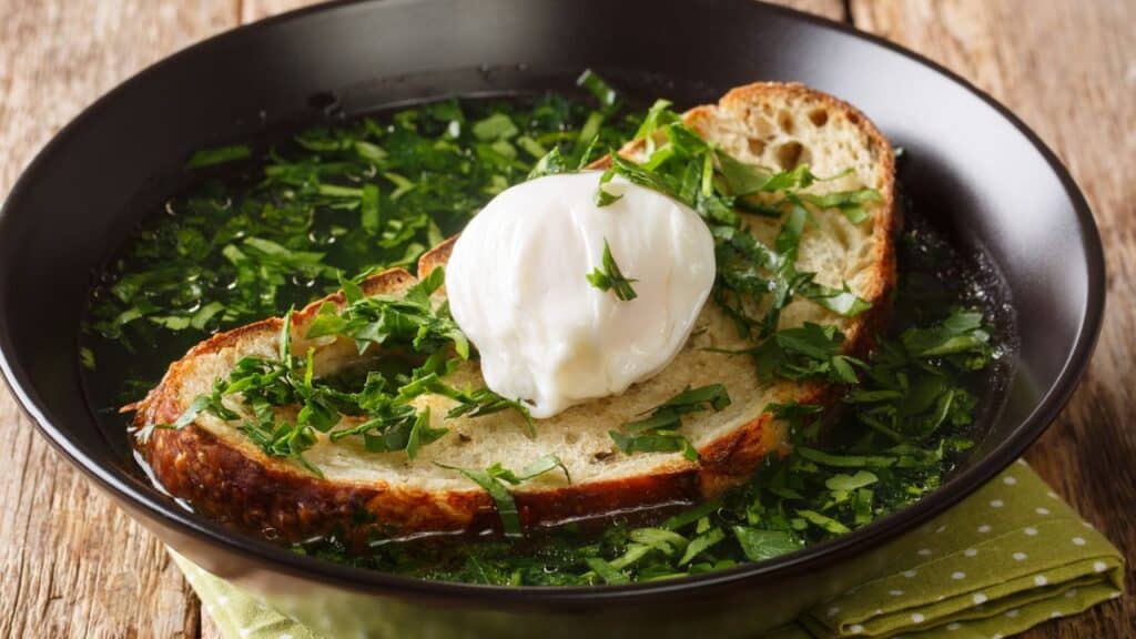 Summer Acorda Soup with cilantro, garlic, homemade bread and poached egg close-up in a bowl on the table