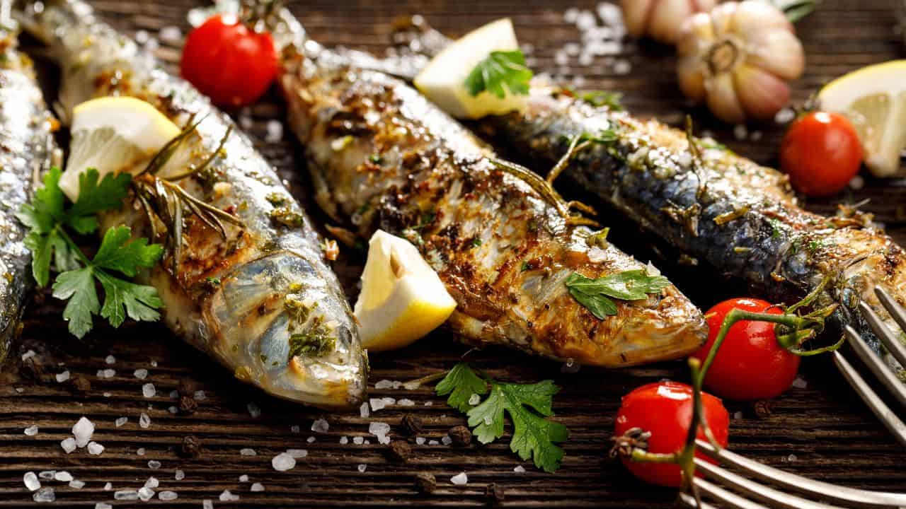 Fried fishes with addition of herbs, spices and lemon slices on a wooden background.