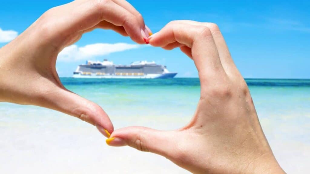Someone's hands making a heart shape around a cruise ship in the distance