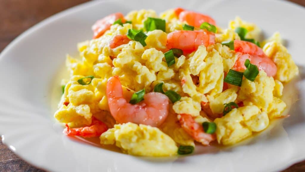 Scrambled eggs with shrimp and green onions in white plate on wooden table background