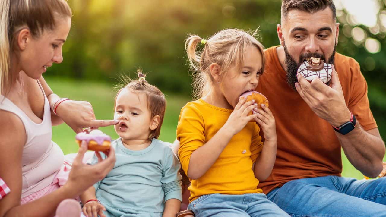 Joyful family picnicking in summer park eating donuts