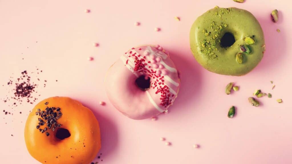 Colorful donuts with icing on pastel pink background. Sweet orange, green, pink doughnuts with pistachio, chocolate.