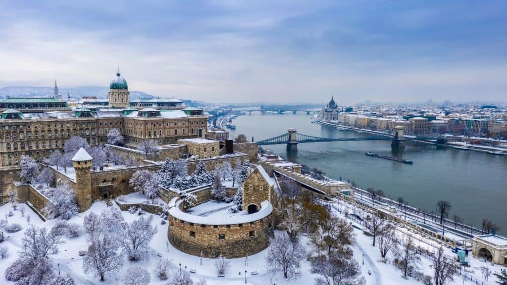 Budapest, Hungary - Aerial panoramic view of the snowy Buda Castle Royal Palace from above with the Szechenyi Chain Bridge and Parliament of Hungary at winter time