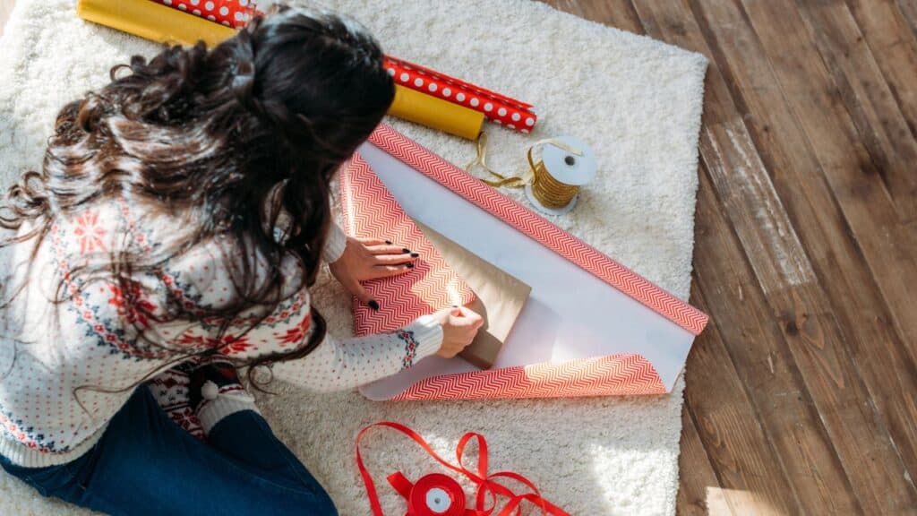 A woman sits on the floor wrapping gifts.