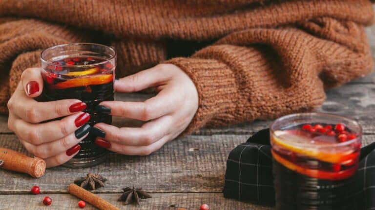 Womans hands in warm sweater holding a cup of mulled wine