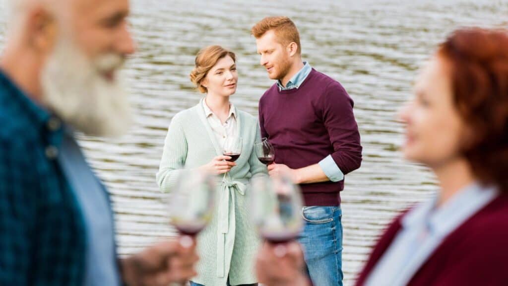 A young couple in the background of the picture having a quiet moment with glasses of wine while an older couple talk closer to the photographer