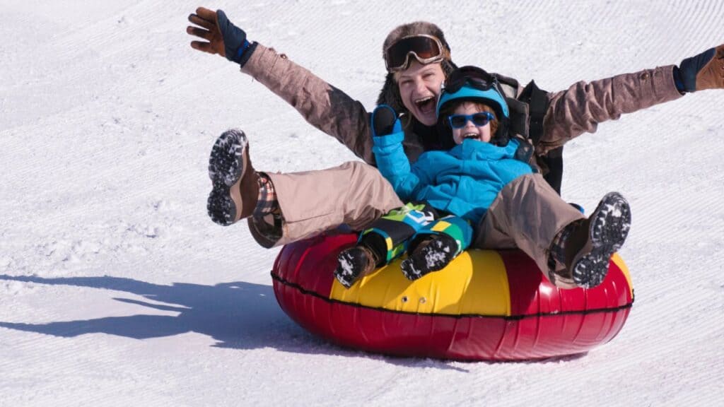 A parent and child snow tubing down a hill