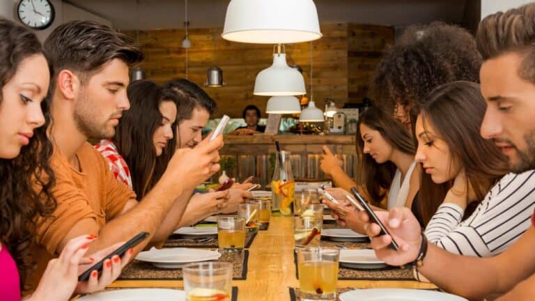 A group of people sitting around the dinner table ignoring each other on their phones.