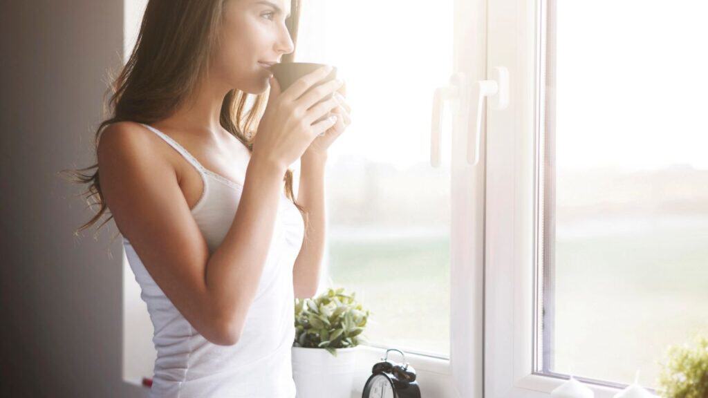 Woman drinking coffee in the morning while she looks out the window.