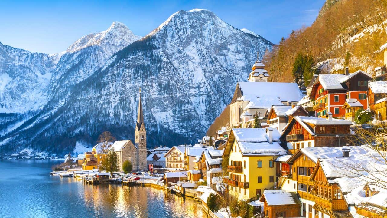Snowy mountainside Hallstatt Austria with a snowy village and church on the water.